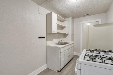 Kitchen featuring white appliances, a textured ceiling, a textured wall, light wood-style floors, and light countertops