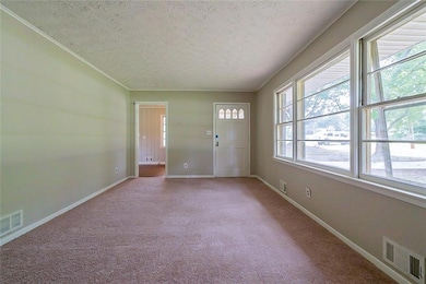 Carpeted empty room featuring a textured ceiling, baseboards, and crown molding