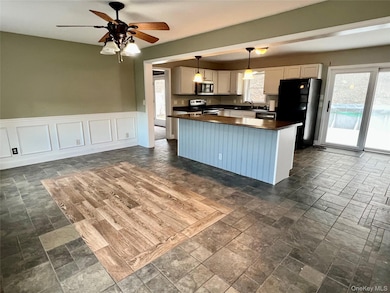Kitchen featuring dark countertops, a kitchen island, appliances with stainless steel finishes, decorative light fixtures, and wainscoting