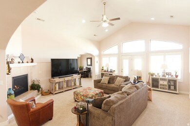 Living area with a fireplace, arched walkways, high vaulted ceiling, light colored carpet, and a ceiling fan