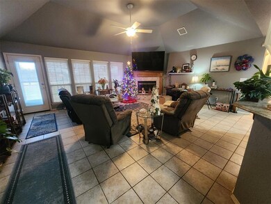 Living room featuring vaulted ceiling, ceiling fan, a brick fireplace, and light tile flooring