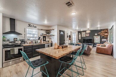 Kitchen with wooden counters, a kitchen bar, stainless steel appliances, wall chimney range hood, and a textured ceiling
