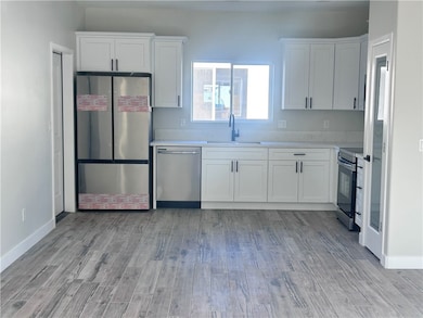 Kitchen featuring stainless steel appliances, white cabinets, light wood-style floors, and light stone countertops