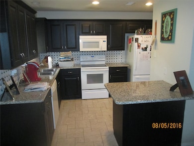 Kitchen with white appliances, light stone countertops, decorative backsplash, dark cabinets, and recessed lighting