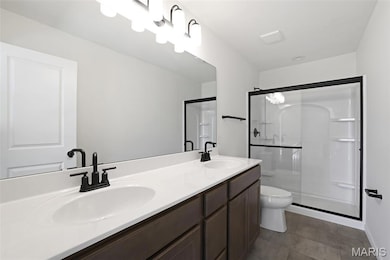 Full bath with a stall shower, double vanity, and dark tile patterned flooring