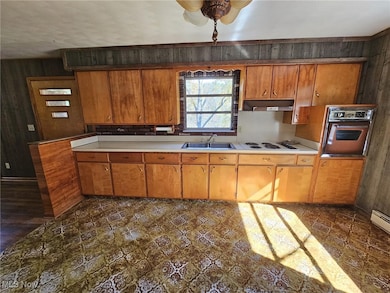 Kitchen featuring light countertops, wood walls, brown cabinetry, under cabinet range hood, and white electric cooktop
