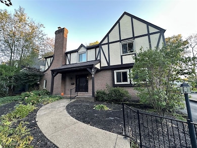 Tudor-style house featuring stucco siding, brick siding, a chimney, and covered porch