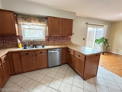 Kitchen featuring brown cabinetry, light tile patterned floors, backsplash, a peninsula, and dishwasher