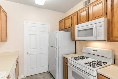 Kitchen featuring white appliances, light countertops, light wood-type flooring, and brown cabinets