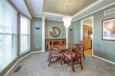 Dining room featuring light carpet, a raised ceiling, crown molding, and a chandelier