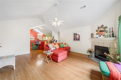 Living area with wood finished floors, a tile fireplace, vaulted ceiling, baseboards, and ceiling fan