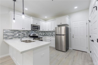 Kitchen with pendant lighting, stainless steel appliances, white cabinetry, kitchen peninsula, and sink