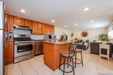 Kitchen with appliances with stainless steel finishes, brown cabinets, light stone countertops, light tile patterned floors, and a kitchen island