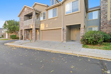 View of front of property with stone siding, stucco siding, an attached garage, a balcony, and driveway