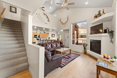 Living room with ceiling fan, light wood-style flooring, high vaulted ceiling, a glass covered fireplace, and stairs