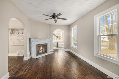 Unfurnished living room featuring dark wood finished floors, arched walkways, a fireplace, a ceiling fan, and stairs