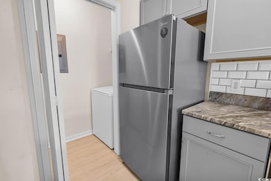 Kitchen with freestanding refrigerator, light wood-type flooring, tasteful backsplash, gray cabinetry, and washer / dryer