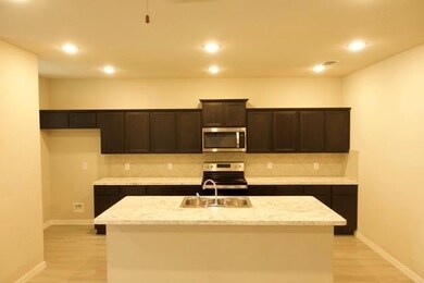 Kitchen featuring stove, tasteful backsplash, light hardwood / wood-style floors, and an island with sink