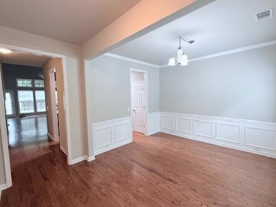 Empty room featuring dark wood finished floors, a chandelier, crown molding, a wainscoted wall, and a decorative wall