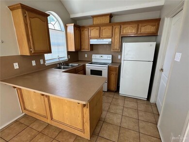 Kitchen featuring white appliances, a peninsula, brown cabinets, light tile patterned floors, and under cabinet range hood