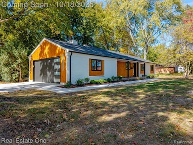 Mid-century home featuring brick siding, view of wooded area, covered porch, a garage, and a chimney