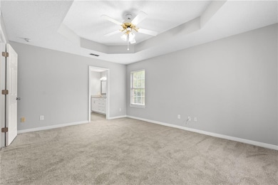 Unfurnished bedroom featuring light carpet, a tray ceiling, baseboards, a textured ceiling, and ensuite bath