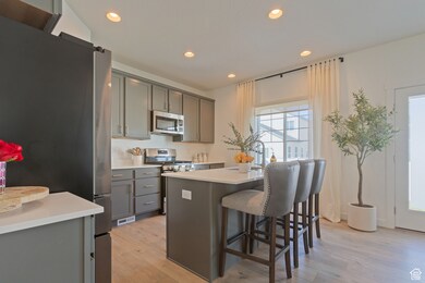 Kitchen featuring appliances with stainless steel finishes, light wood-type flooring, an island with sink, recessed lighting, and a kitchen breakfast bar