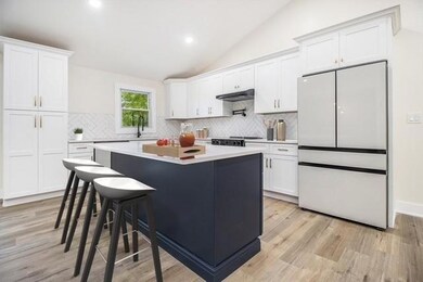 Kitchen with freestanding refrigerator, decorative backsplash, lofted ceiling, a center island, and white cabinetry