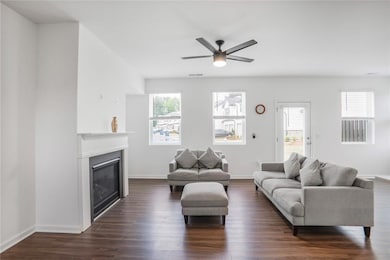 Living room with dark wood-style flooring, a ceiling fan, a glass covered fireplace, and baseboards