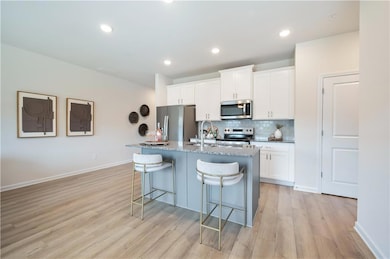 Kitchen with backsplash, white cabinets, stainless steel appliances, dark stone countertops, and a kitchen island with sink