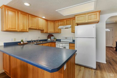 Kitchen featuring white appliances, dark countertops, a peninsula, arched walkways, and under cabinet range hood