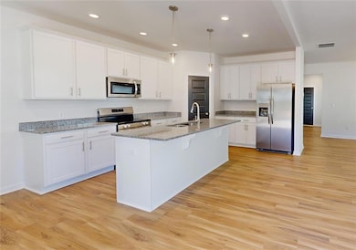 Kitchen featuring sink, white cabinets, hanging light fixtures, and appliances with stainless steel finishes