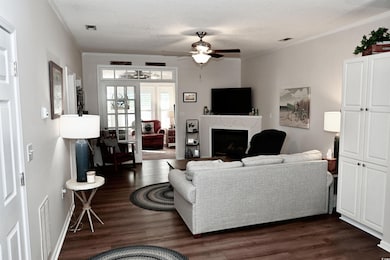 Living area featuring ceiling fan, a fireplace, dark wood finished floors, and crown molding