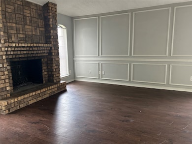 Unfurnished living room with a brick fireplace, dark wood-type flooring, a decorative wall, and a textured ceiling