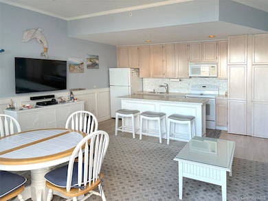 Kitchen featuring white appliances, ornamental molding, a breakfast bar, backsplash, and an island with sink