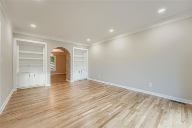 Unfurnished room featuring built in shelves, ornamental molding, arched walkways, light wood-type flooring, and recessed lighting