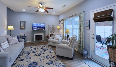 Living area featuring visible vents, a warm lit fireplace, wood finished floors, baseboards, and ceiling fan