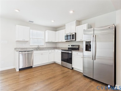 Kitchen with appliances with stainless steel finishes, white cabinets, light wood-style flooring, light stone countertops, and recessed lighting