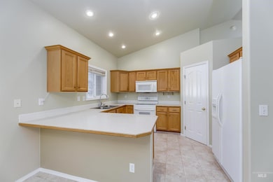 Kitchen with white appliances, a peninsula, light countertops, lofted ceiling, and recessed lighting