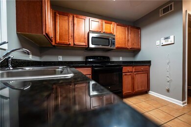 Kitchen with black electric range, stainless steel microwave, a sink, light tile patterned floors, and dark countertops
