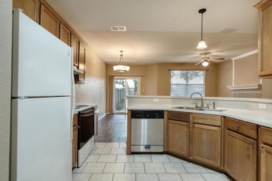 Kitchen featuring white appliances, brown cabinetry, light countertops, decorative light fixtures, and a ceiling fan