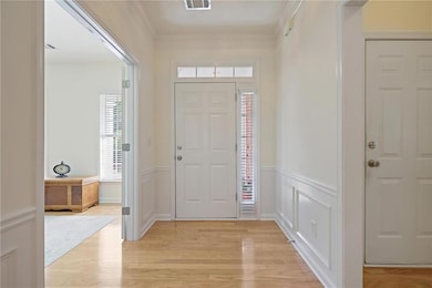 Foyer featuring light wood finished floors, crown molding, wainscoting, and a decorative wall
