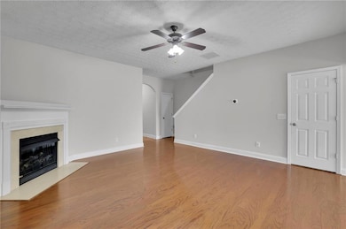 Unfurnished living room with light wood-style floors, arched walkways, a fireplace, a textured ceiling, and a ceiling fan
