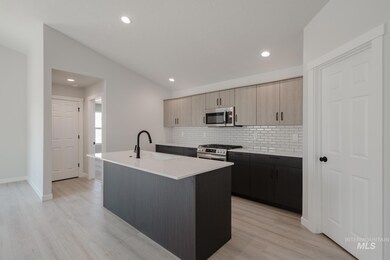 Kitchen with a center island with sink, backsplash, stainless steel appliances, light stone counters, and light wood-type flooring