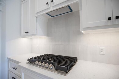 Kitchen view of stainless steel gas stovetop, white cabinets, decorative backsplash, and range hood