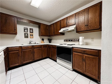 Kitchen featuring under cabinet range hood, range with electric cooktop, light countertops, and a sink