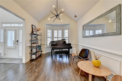 Entrance foyer featuring a chandelier, a decorative wall, dark wood-style flooring, wainscoting, and vaulted ceiling