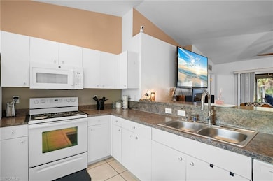 Kitchen featuring white appliances, white cabinets, light tile patterned floors, dark countertops, and vaulted ceiling