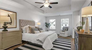 Bedroom with a tray ceiling, dark wood-style floors, and a ceiling fan