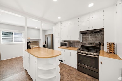 Kitchen featuring open shelves, backsplash, appliances with stainless steel finishes, light countertops, and white cabinetry
